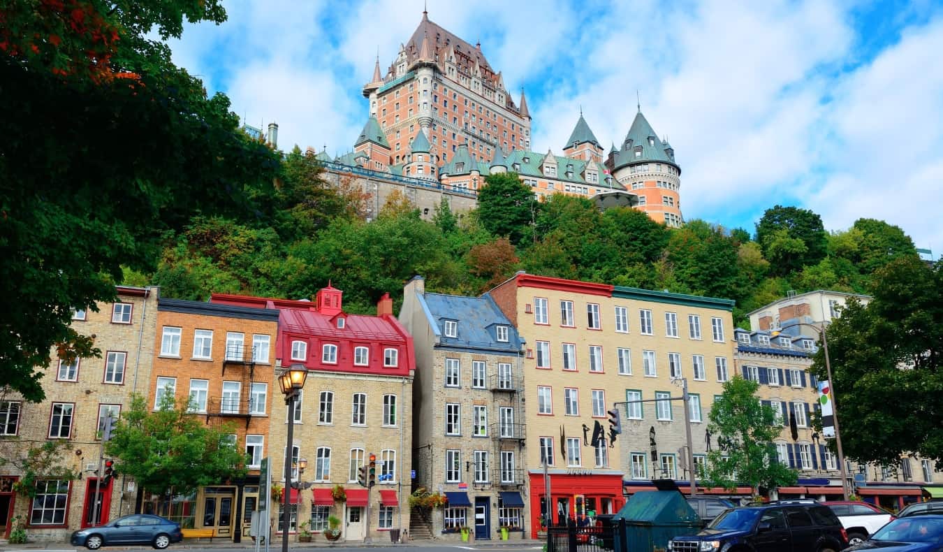 uma fileira de casas de pedra com telhados de cores vivas, enquanto o Castelo Frontenac surge no fundo de Vieux-Québec, na cidade de Quebec, Canadá