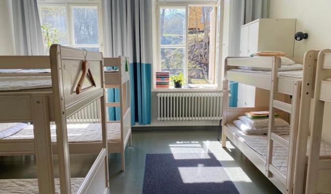 Dormitório do Hostel Suomenlinna em Helsinque, Finlândia, com beliches de madeira branca e luz solar natural entrando