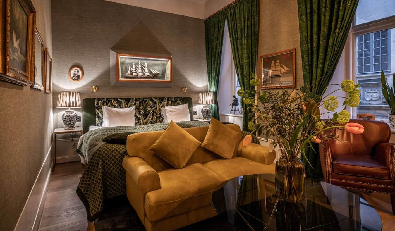 Quarto luxuoso com sofá de veludo, poltrona de couro, cortinas esmeraldas nas janelas e paredes revestidas de tecido no Collectors Victory Hotel em Estocolmo, Suécia