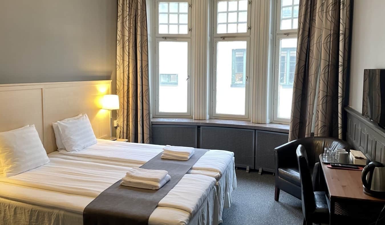 Quarto decorado de forma simples, com cama de casal e janelas grandes no Unique Hotel em Estocolmo, Suécia